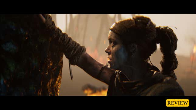 Senua places her hand on a stone while looking up.