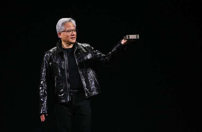 Jensen Huang wearing a shiny black leather jacket holding up a small device